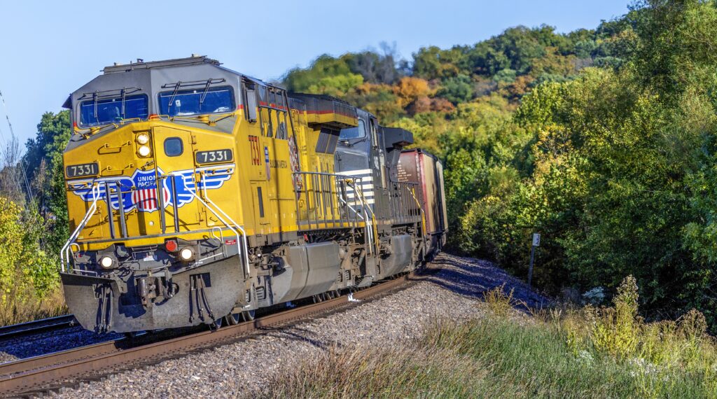 Union Pacific and Norfolk Southern locomotives traveling through a wooded landscape