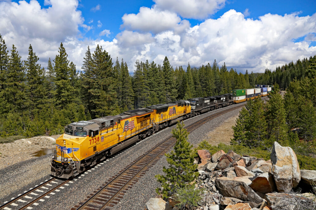Union Pacific and Norfolk Southern locomotives lead an intermodal freight train through a forest near Troy, California.