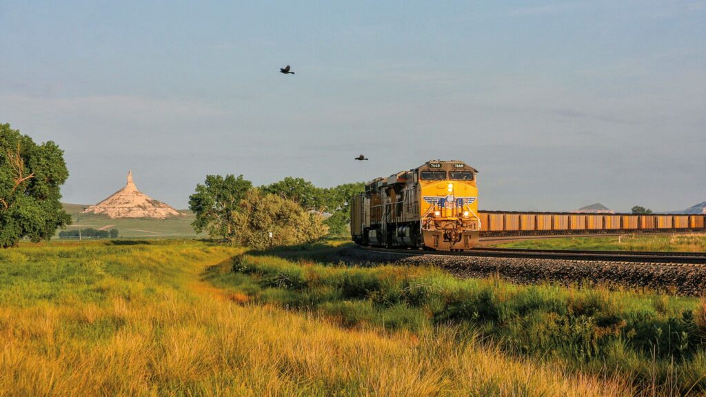 Union Pacific freight train traveling through green grassland near Chimney Rock