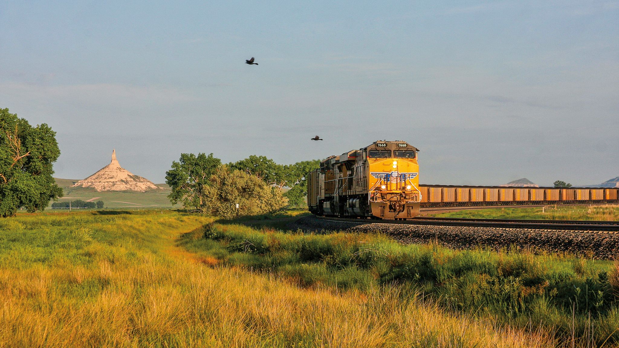 Union Pacific freight train traveling through green grassland near Chimney Rock