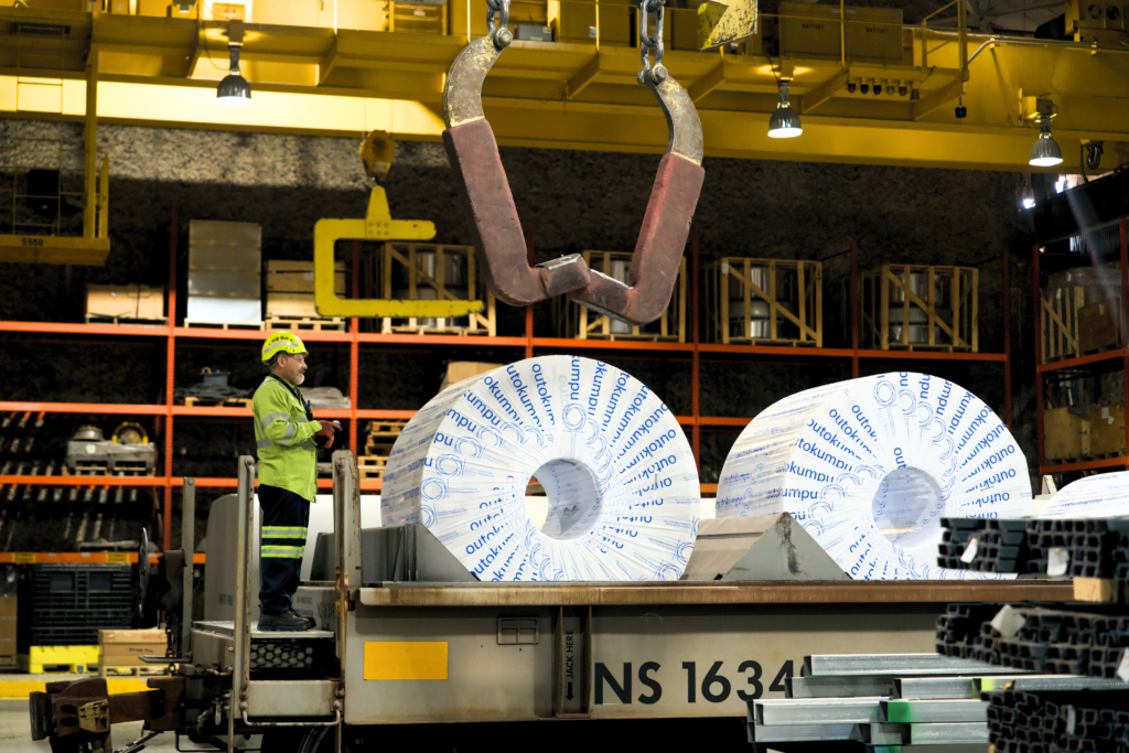 Worker beside wrapped steel coils on a railcar inside a transloading facility.
